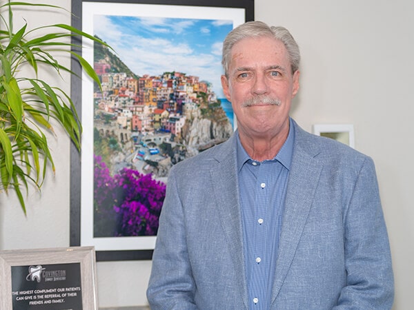 One of our leading dentists, Dr. Otto Hanssen wearing a shirt and suit jacket standing next to the reception desk smiling